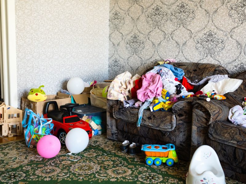 A living room in a home filled with various old toys, clothes, and other household garbage.